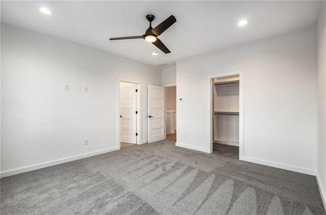 unfurnished bedroom with ceiling fan, a closet, dark colored carpet, and a walk in closet