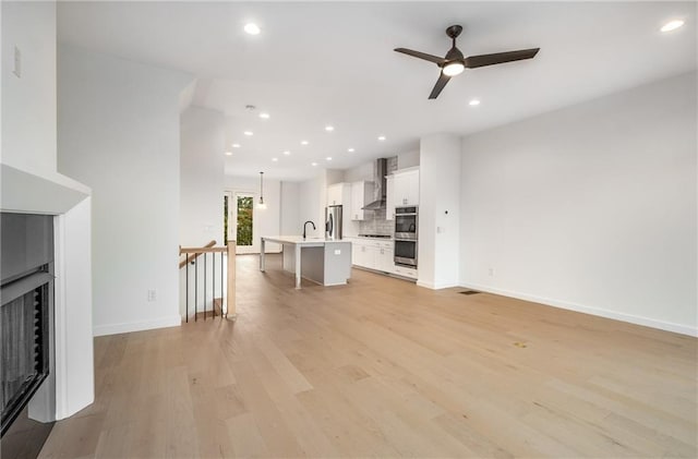 unfurnished living room featuring light wood-type flooring, ceiling fan, and sink