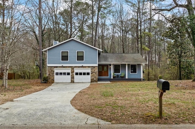 split level home featuring a porch, a front yard, stone siding, and concrete driveway