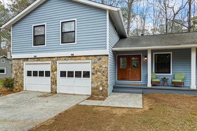 tri-level home with driveway, a shingled roof, stone siding, an attached garage, and covered porch