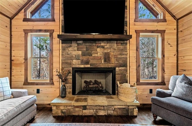 living area with vaulted ceiling, wooden ceiling, wooden walls, hardwood / wood-style flooring, and a stone fireplace