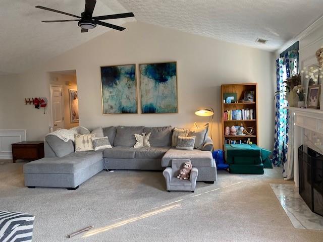 carpeted living room with ceiling fan, a fireplace, vaulted ceiling, and a textured ceiling