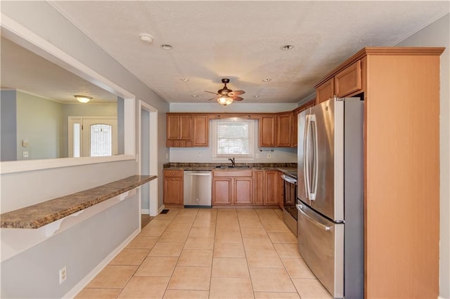 kitchen with light tile patterned floors, brown cabinetry, ceiling fan, stainless steel appliances, and a sink