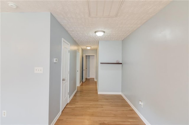 hallway featuring light wood-style floors, baseboards, visible vents, and a textured ceiling