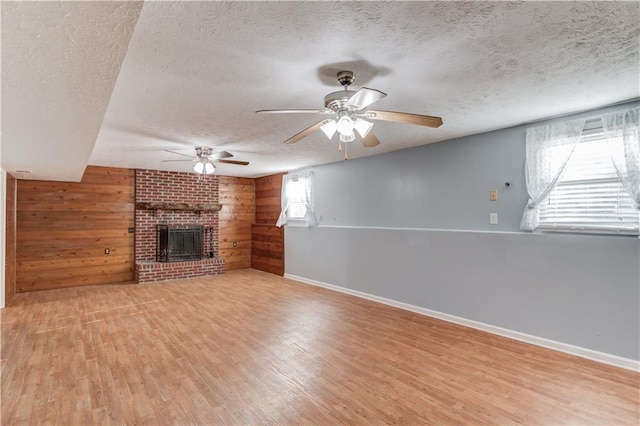 unfurnished living room featuring light wood-type flooring, a fireplace, wood walls, and a textured ceiling