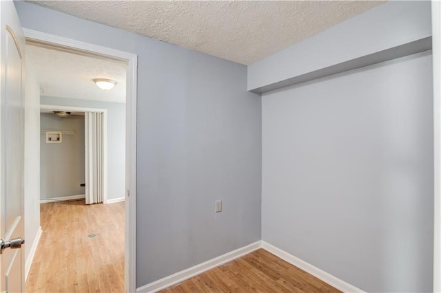 empty room featuring baseboards, a textured ceiling, and light wood finished floors