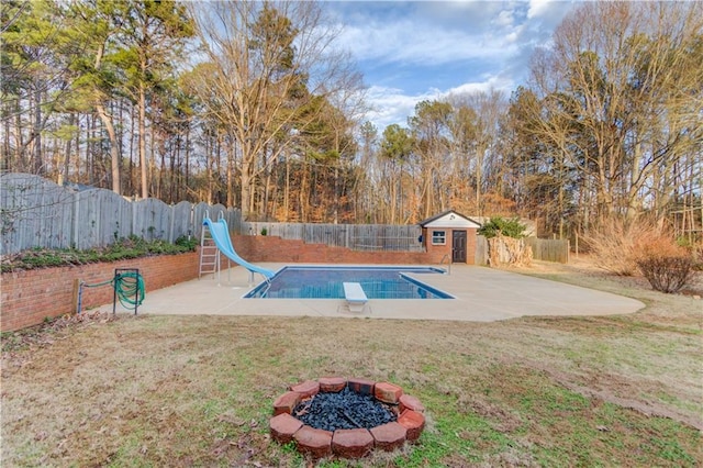 view of swimming pool with a water slide, a fenced backyard, a fire pit, an outdoor structure, and a lawn