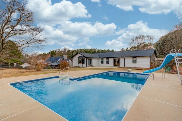 pool with a diving board, a water slide, a patio area, and fence