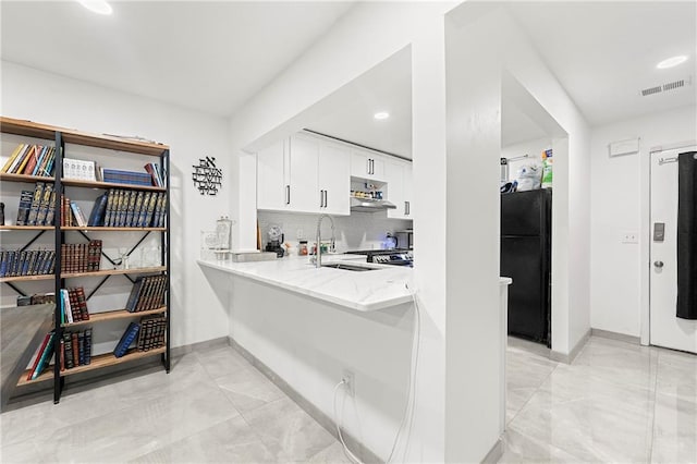 kitchen with tasteful backsplash, light stone counters, black fridge, sink, and white cabinetry