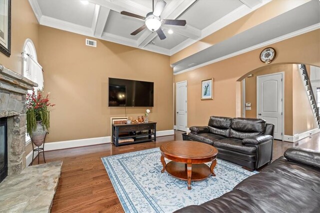 living room with dark wood-type flooring, ceiling fan, ornamental molding, a fireplace, and beam ceiling