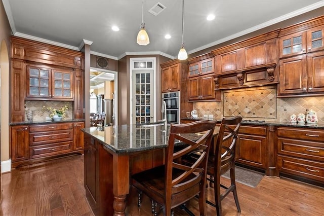 kitchen with a breakfast bar, a center island, dark stone counters, decorative light fixtures, and dark hardwood / wood-style flooring