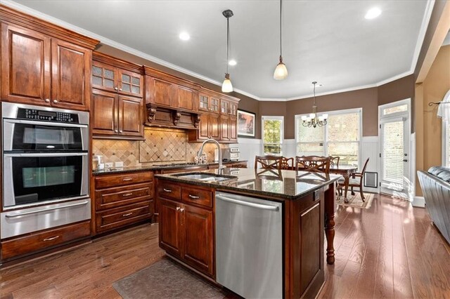 kitchen with stainless steel appliances, sink, decorative light fixtures, dark hardwood / wood-style floors, and an island with sink