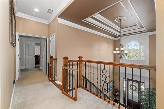 hall with ornamental molding, light carpet, a tray ceiling, and a chandelier