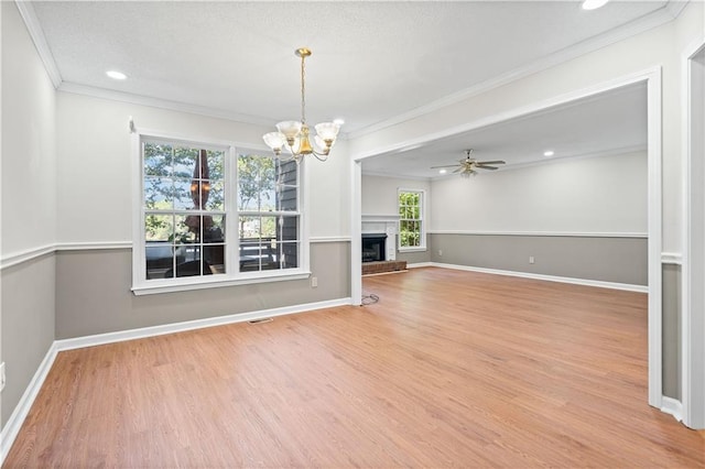 unfurnished living room with ceiling fan with notable chandelier, wood finished floors, crown molding, baseboards, and a brick fireplace