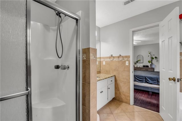 bathroom with vanity, a shower with shower door, tile patterned floors, and tile walls