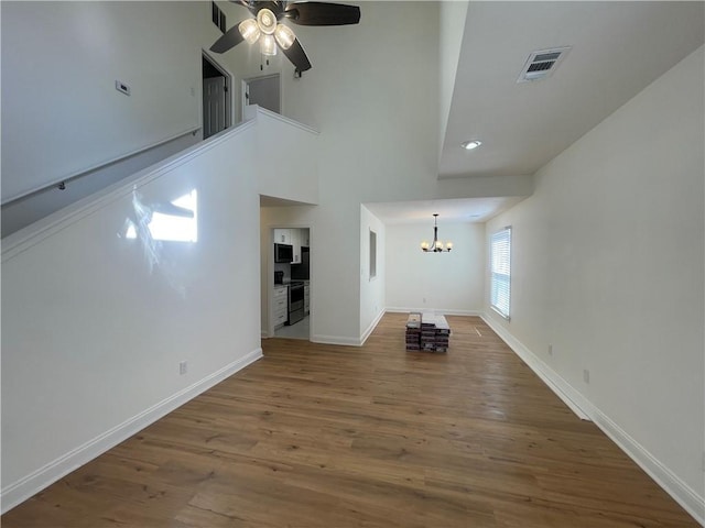 unfurnished living room with baseboards, visible vents, wood finished floors, and ceiling fan with notable chandelier