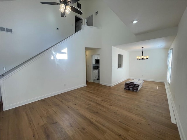 unfurnished living room featuring baseboards, visible vents, wood finished floors, and ceiling fan with notable chandelier