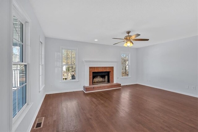 unfurnished living room with ceiling fan, plenty of natural light, dark hardwood / wood-style floors, and a brick fireplace