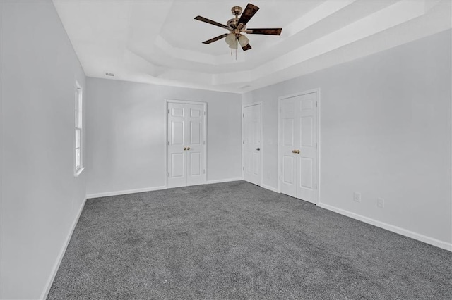 spare room featuring a tray ceiling, ceiling fan, and dark carpet