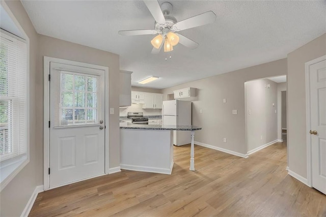 kitchen with freestanding refrigerator, a peninsula, stainless steel gas stove, and light wood finished floors