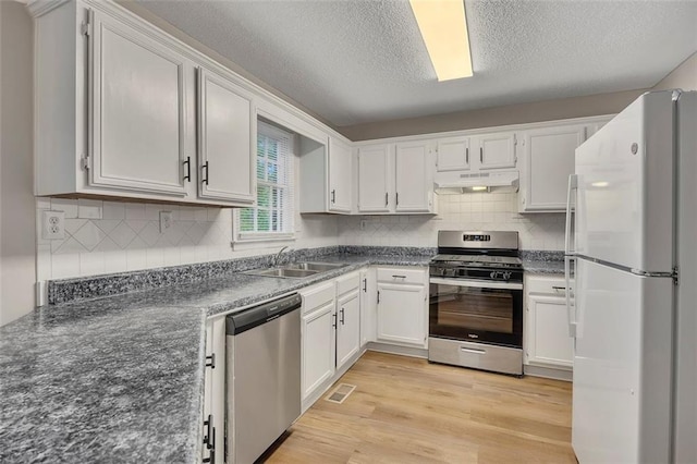 kitchen with a sink, dark countertops, stainless steel appliances, under cabinet range hood, and decorative backsplash