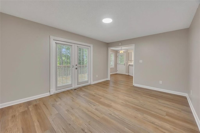 spare room with a wealth of natural light, baseboards, french doors, and light wood-style floors