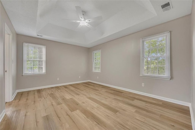 spare room featuring a raised ceiling, light wood finished floors, visible vents, and a wealth of natural light
