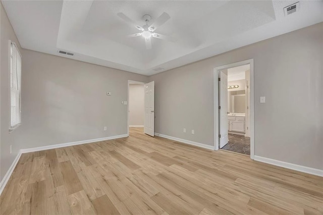 unfurnished bedroom with a tray ceiling, baseboards, light wood-type flooring, and visible vents
