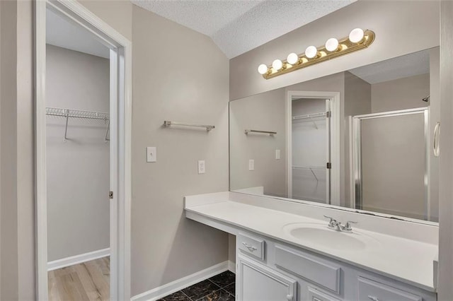 bathroom with a stall shower, baseboards, vanity, and a walk in closet