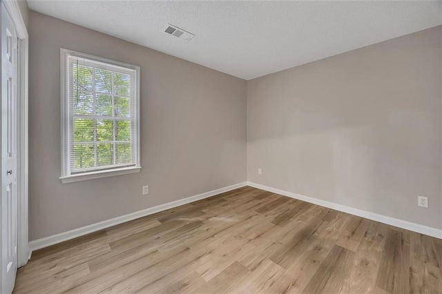 spare room featuring a textured ceiling, visible vents, wood finished floors, and baseboards