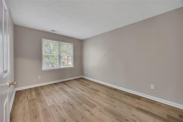 unfurnished room featuring baseboards, visible vents, a textured ceiling, and wood finished floors
