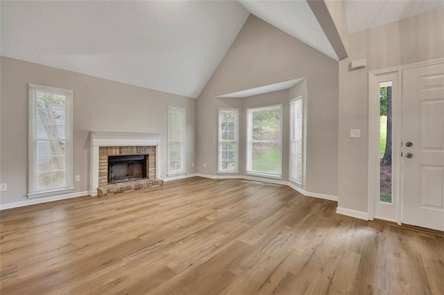 unfurnished living room with light wood finished floors, a brick fireplace, baseboards, and high vaulted ceiling