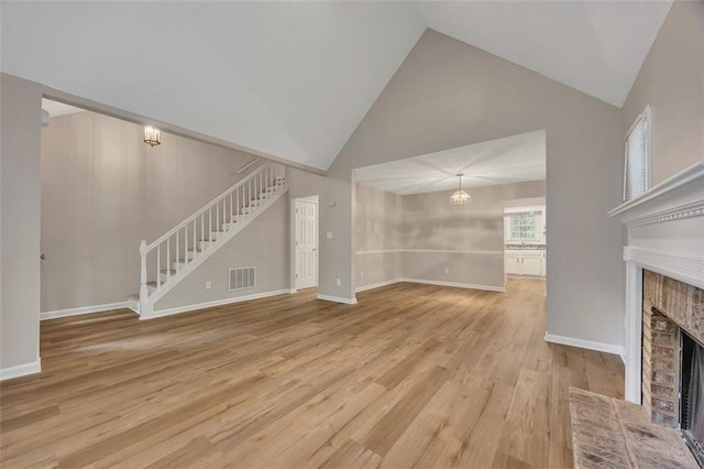 unfurnished living room with an inviting chandelier, visible vents, high vaulted ceiling, stairway, and a fireplace