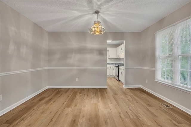 unfurnished dining area featuring baseboards, light wood-style flooring, visible vents, and a textured ceiling