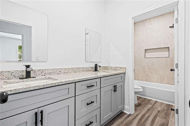 full bathroom with double vanity, a sink, toilet, and wood finished floors