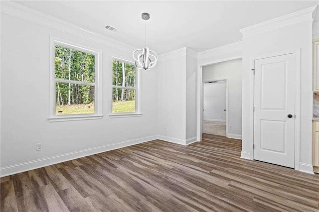 unfurnished dining area featuring baseboards, visible vents, ornamental molding, wood finished floors, and a chandelier