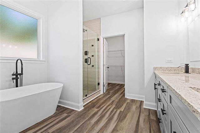 bathroom with wood finished floors, vanity, baseboards, a spacious closet, and a shower stall