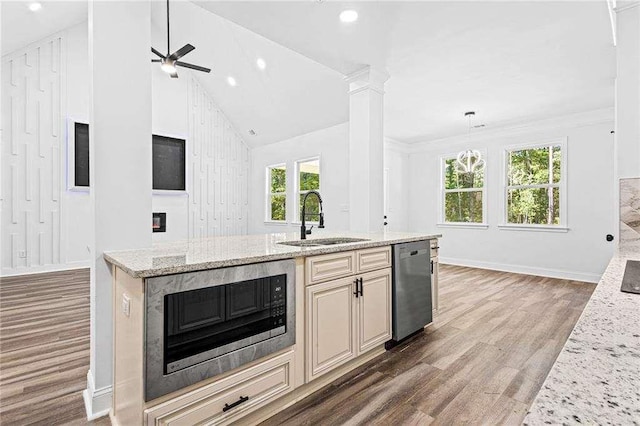 kitchen with wood finished floors, light stone countertops, stainless steel appliances, ornate columns, and a sink