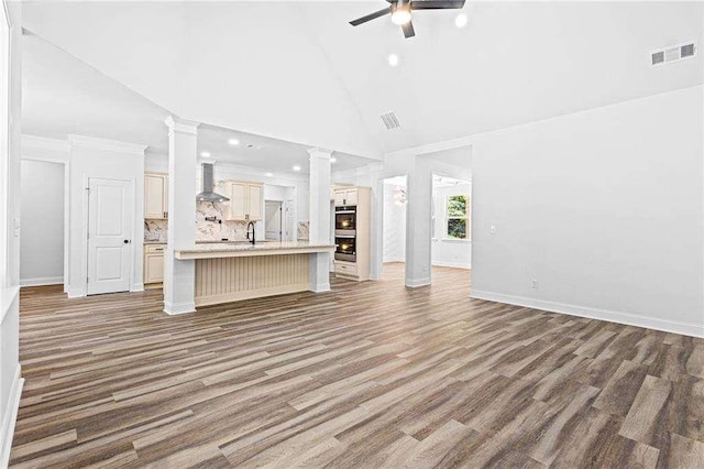 unfurnished living room featuring a sink, a ceiling fan, wood finished floors, visible vents, and ornate columns