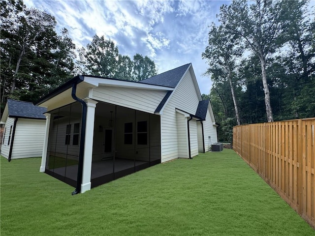 rear view of property featuring roof with shingles, a lawn, central AC unit, and fence