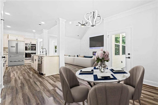 dining space with dark wood-style flooring, a notable chandelier, crown molding, ornate columns, and baseboards