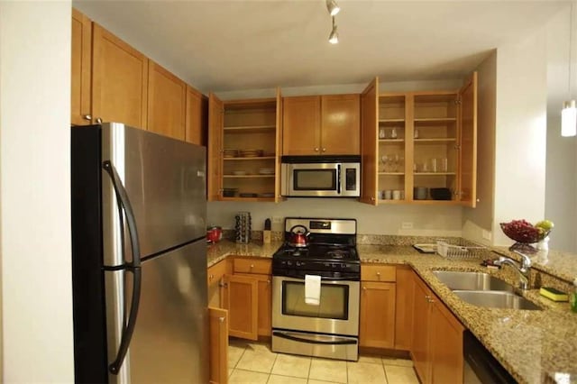 kitchen with appliances with stainless steel finishes, light stone counters, light tile patterned floors, track lighting, and sink