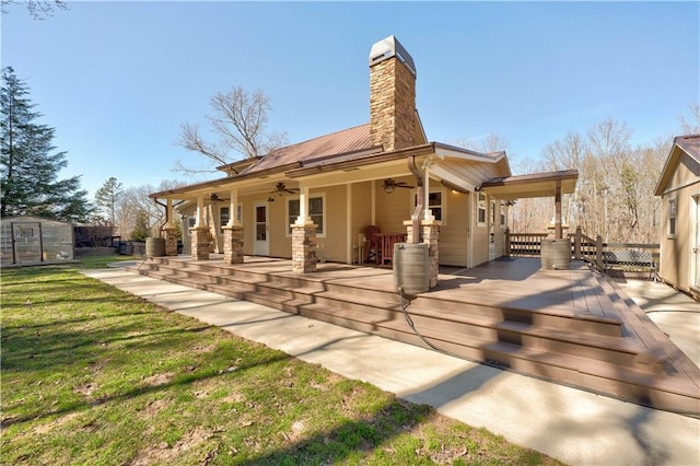 rear view of house featuring metal roof, an outdoor structure, a ceiling fan, a lawn, and a chimney