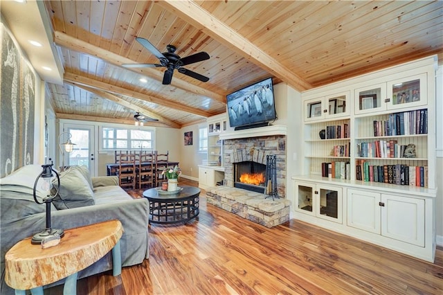 living room with vaulted ceiling with beams, a stone fireplace, wood finished floors, and wood ceiling