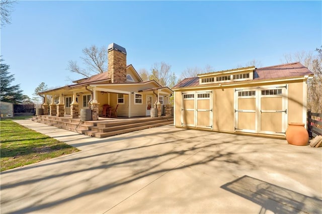 rear view of property with an outbuilding, a chimney, stucco siding, a storage shed, and central AC unit