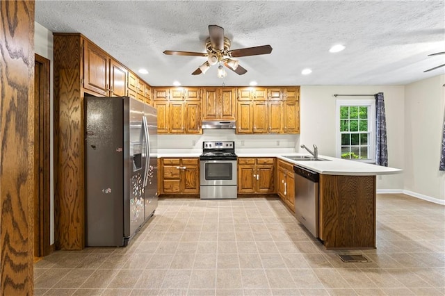 kitchen with stainless steel appliances, ceiling fan, a peninsula, a sink, and brown cabinetry