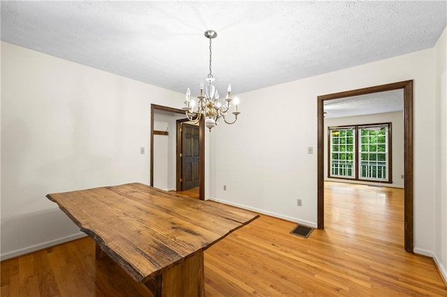 unfurnished dining area featuring a chandelier, light wood finished floors, baseboards, and a textured ceiling