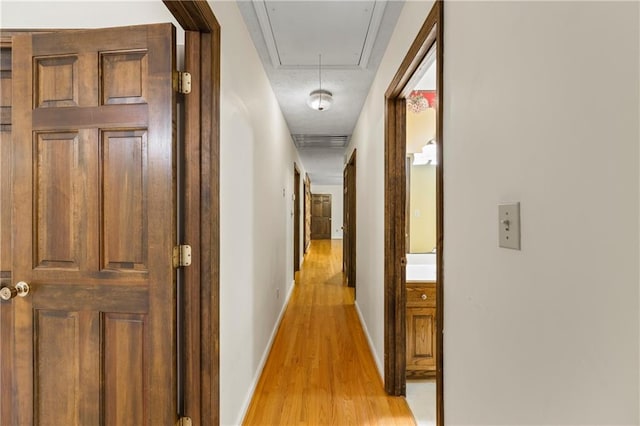 corridor with light wood finished floors, attic access, and baseboards