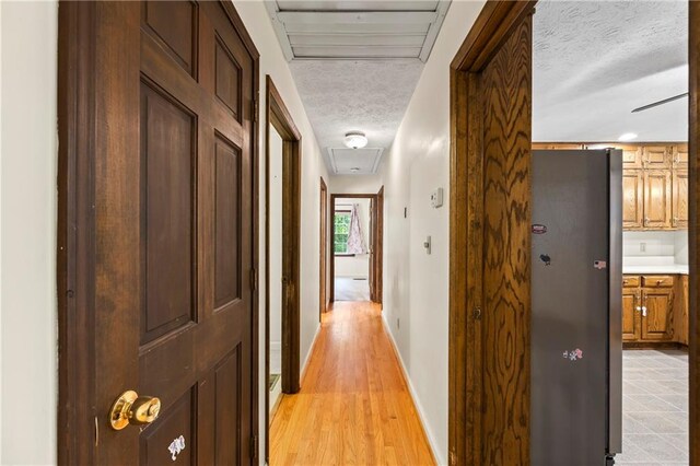 hall with attic access, a textured ceiling, baseboards, and light wood finished floors