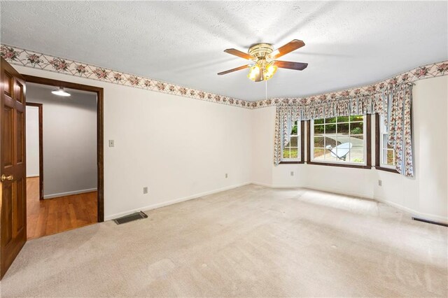 spare room featuring light carpet, a ceiling fan, baseboards, and a textured ceiling